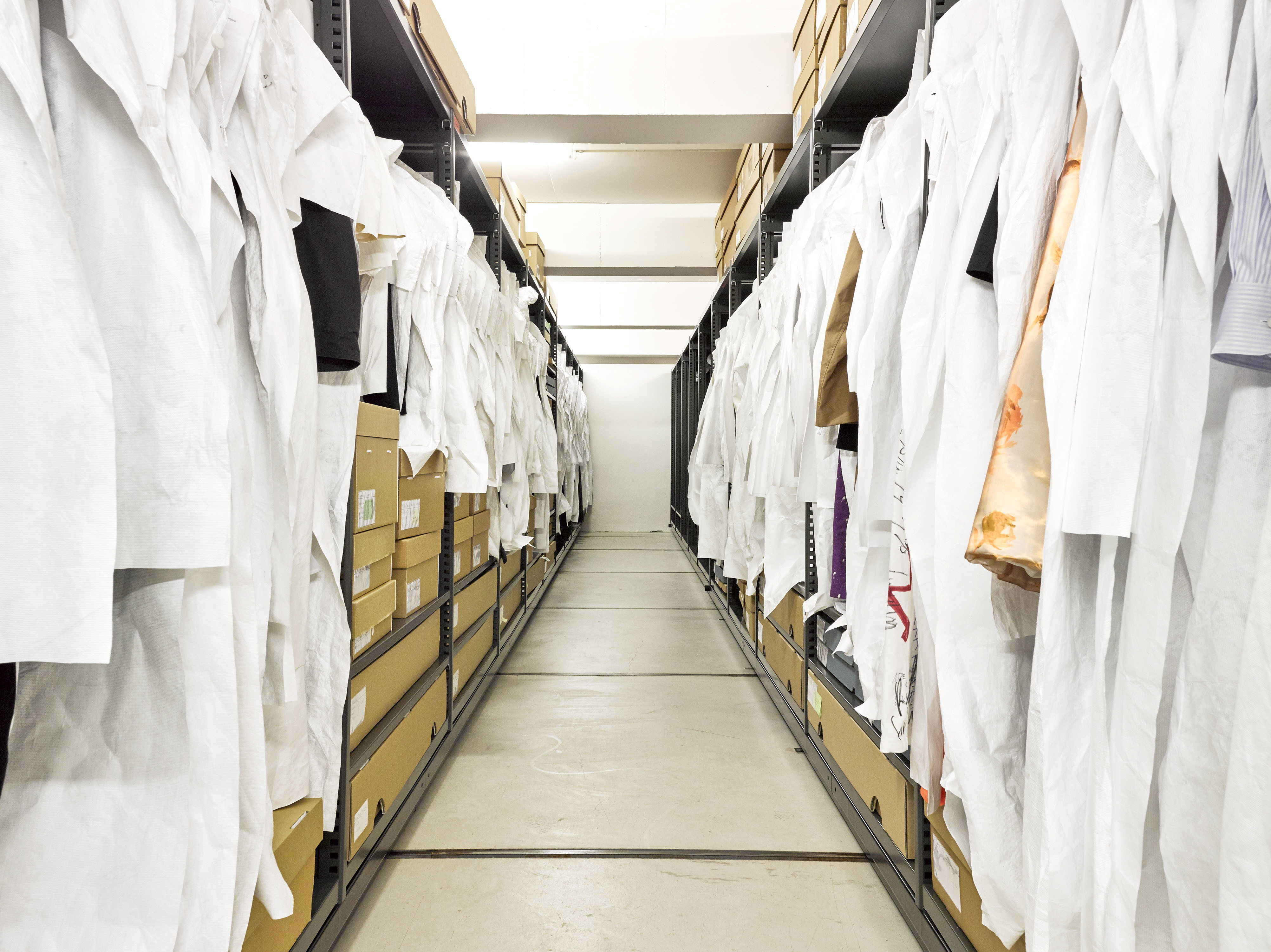 Image of the collection depot in MoMu with wardrobes on both sides in which museum objects hang or lie down in bags or boxes.
